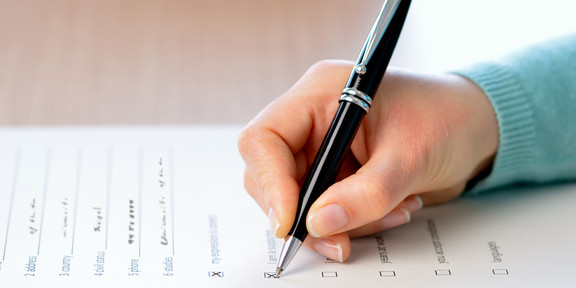 A hand holding a pen fills out a survey questionnaire.